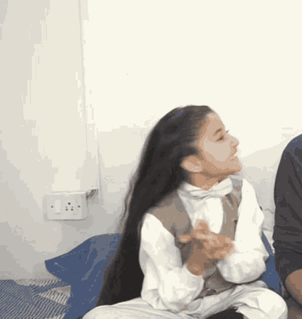 a girl with long black hair is sitting on a bed with a man