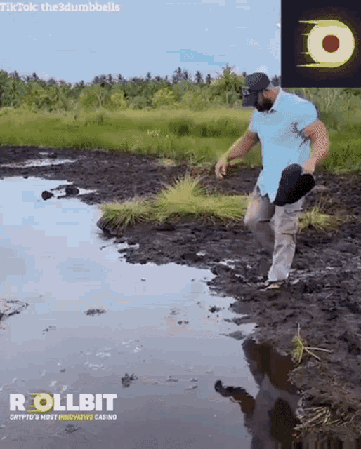 a man in a blue shirt is walking through a muddy field .
