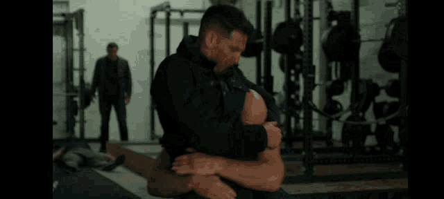 a man is holding another man 's head in a gym while another man stands in the background .