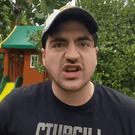 a man wearing a hat and a black shirt is making a funny face in front of a playground .