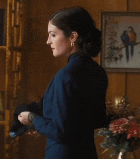 a woman in a blue jacket stands in front of framed pictures