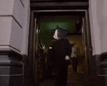 a man with a cat on his head is walking through a doorway in a dark hallway .