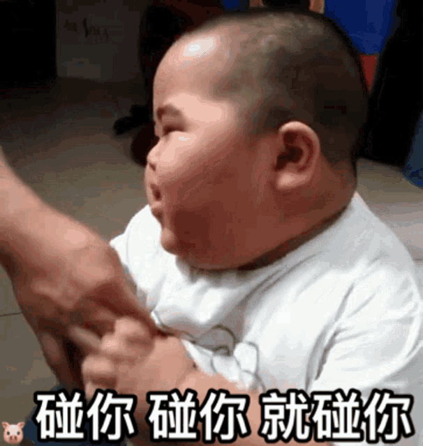 a baby in a white shirt is being held by a person with chinese writing on it