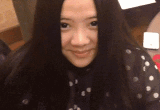 a woman with long black hair is smiling and wearing a black and white polka dot shirt