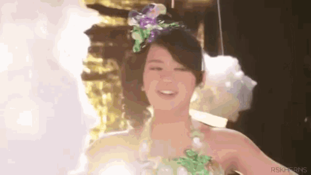 a woman in a green dress with flowers in her hair is smiling and looking at the camera .