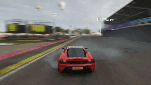 a red sports car is driving down a road with a festival site visible in the corner