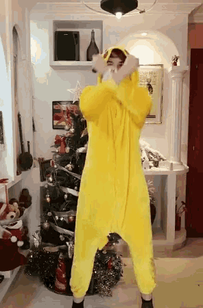 a person wearing a yellow onesie is standing in front of a christmas tree