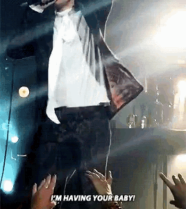 a man in a suit is singing into a microphone while a crowd applauds .