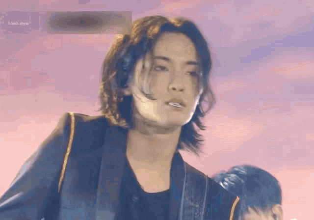 a young man with long hair is playing a guitar on stage .