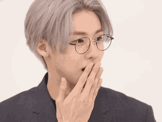 a man wearing glasses and covering his mouth with his hand