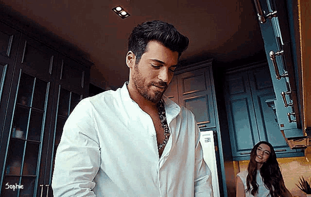 a man in a white shirt is cooking in a kitchen while a woman looks on .