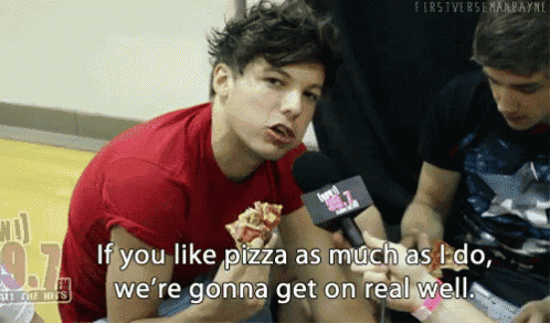 a man in a red shirt is talking into a microphone while holding a pizza
