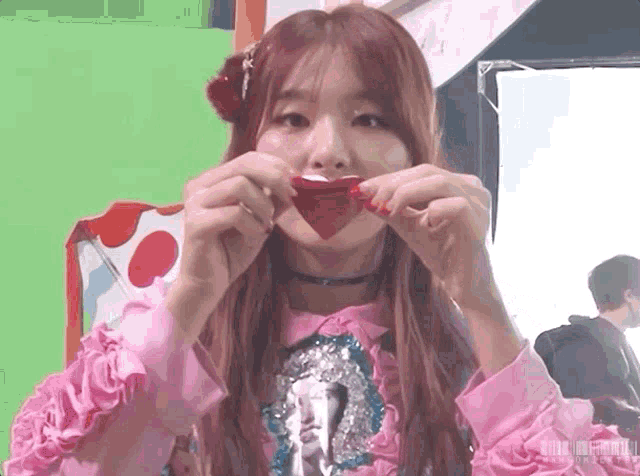 a woman in a pink shirt is eating a red heart shaped candy