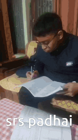 a young man is sitting at a table writing in a notebook .