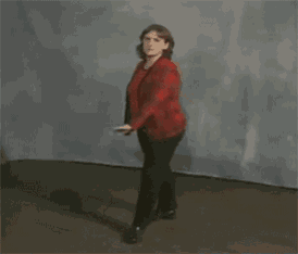 a woman in a red shirt and black pants is dancing in a room with her arms outstretched .