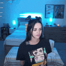 a woman wearing a black t-shirt with a picture of a girl on it stands in a bedroom