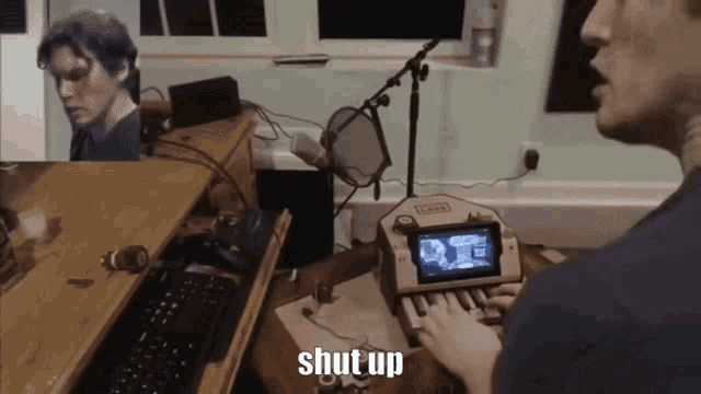 a man sitting at a desk with a keyboard and a device that says shut up on it