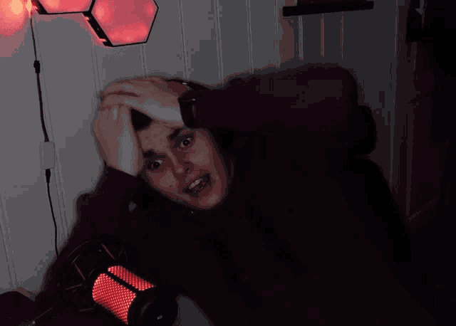 a man sitting in front of a microphone with red lights on the wall behind him
