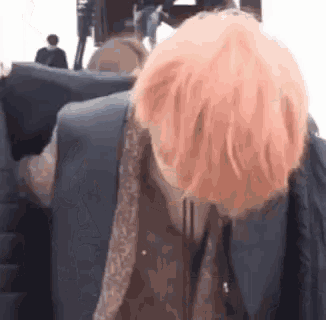 a person with pink hair is sitting on a couch and covering their face .