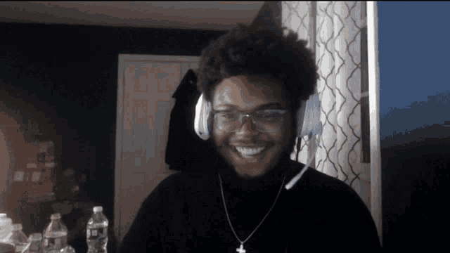 a man wearing headphones and a necklace with a cross on it smiles