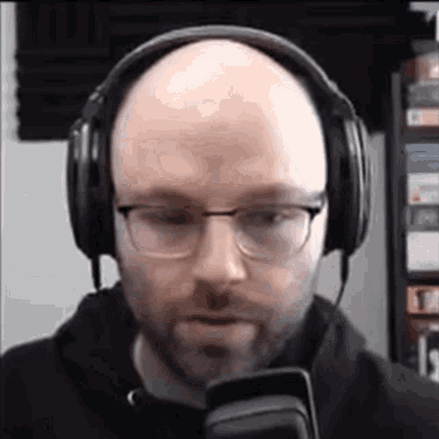 a bald man with glasses and headphones is looking at a cell phone .