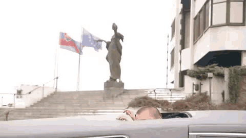 a statue of a woman stands in front of a building with two flags
