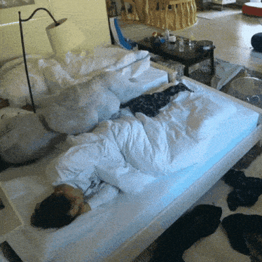 a person laying on a bed with white sheets and a lamp