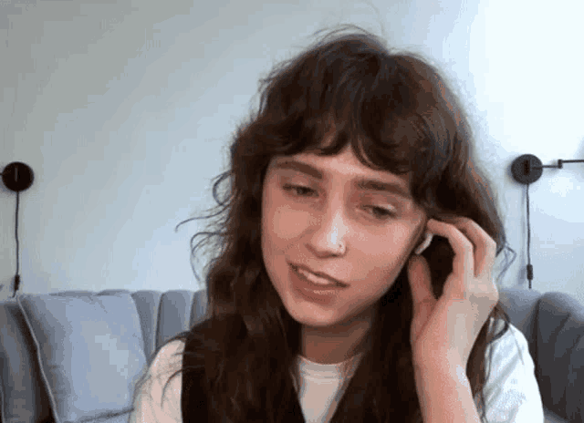 a woman is sitting on a couch wearing headphones and talking on a cell phone .