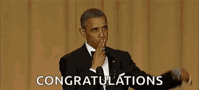 barack obama is giving a speech in front of a microphone while covering his mouth with his hand .