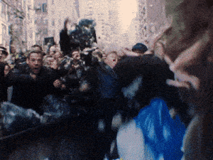 a crowd of people are gathered on a street and one of them has a blue bag