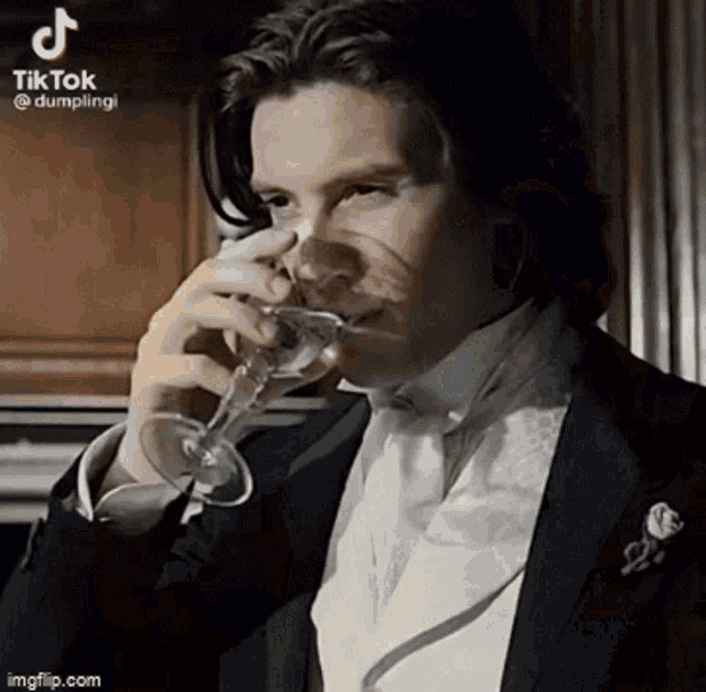 a man in a tuxedo is drinking from a glass