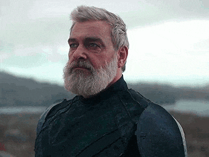 a man with a beard and gray hair is wearing armor and looking to the side .