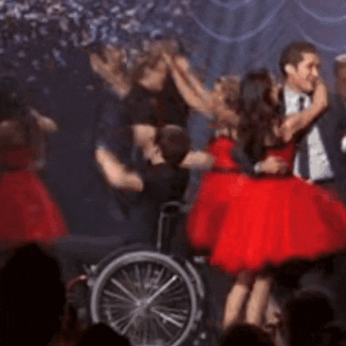 a man in a wheelchair is hugging two women in red dresses on a stage