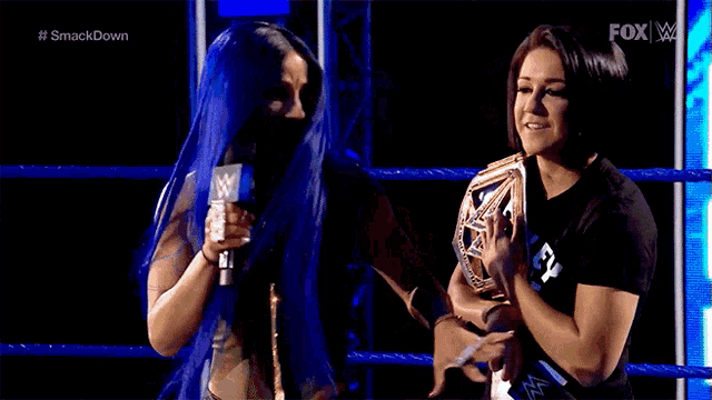 a woman with blue hair is talking to another woman in a wrestling ring while holding a microphone .