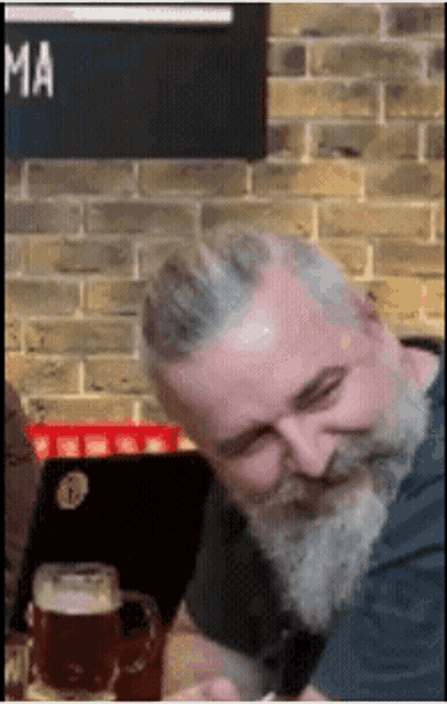 a man with a beard sits at a table with a glass of beer