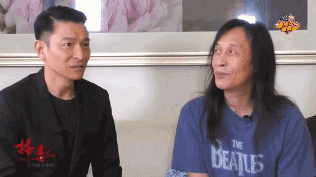two men sitting next to each other one wearing a blue beatles shirt