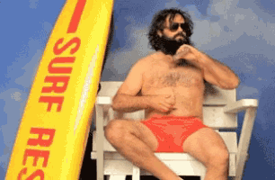 a shirtless man sits in a lifeguard chair next to a yellow surfboard that says surf rescue