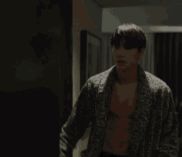 a shirtless man in a robe is standing in a dark room