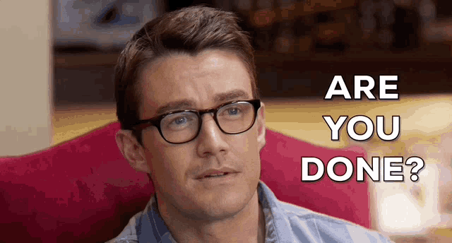 a man wearing glasses is sitting on a couch with the words " are you done " behind him