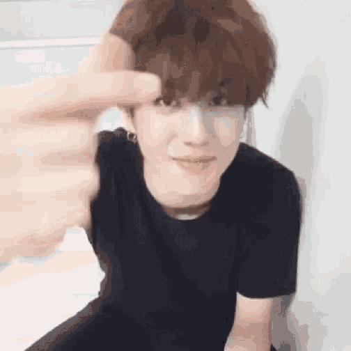 a young man in a black t-shirt is giving a thumbs up .