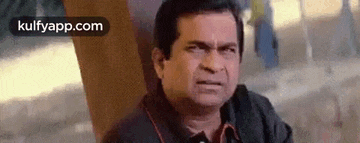 a man is making a funny face while sitting in front of a wooden wall .
