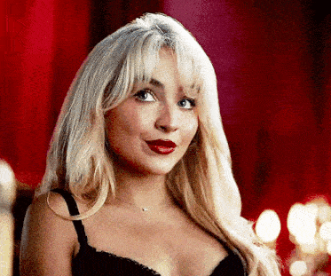 a woman with blonde hair and red lips is wearing a black bra and necklace .