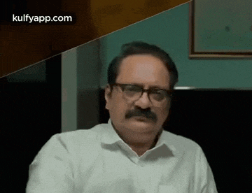 a man with glasses and a mustache is sitting in front of a wall .