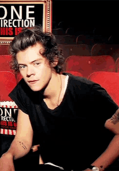 a young man sits in front of a sign that says one direction his is