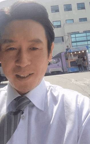 a man in a white shirt and tie is smiling in front of a food truck