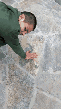 a young boy wearing a green sweatshirt is touching a stone wall