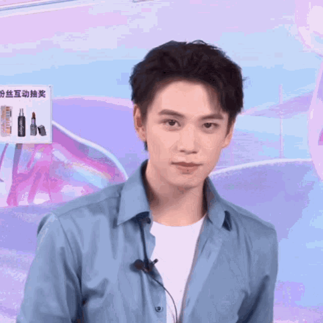 a man wearing a blue shirt with a microphone around his neck looks at the camera