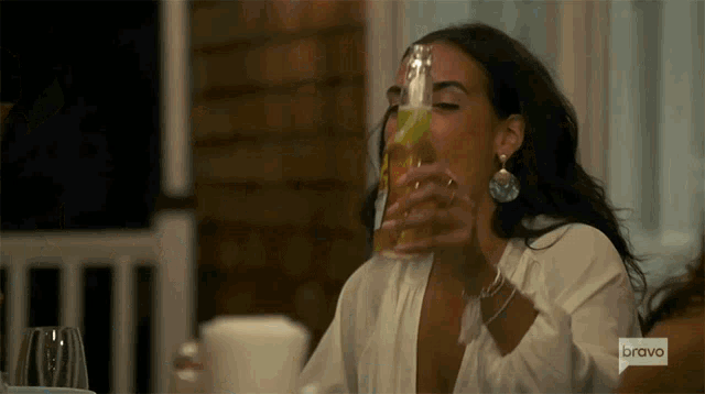 a woman is drinking a beer from a bottle with the word bravo on the bottom