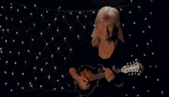 a woman is playing a guitar in a dark room with christmas lights behind her .