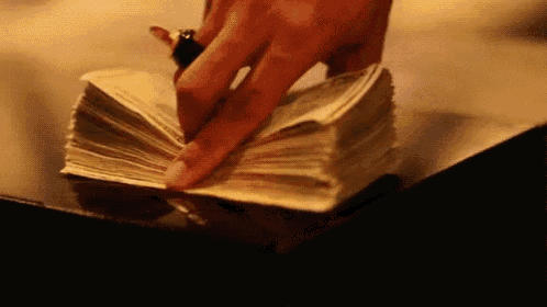 a woman 's hand is reaching into a pile of money on a table .